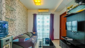 A modern living room with a sofa, a water dispenser, a flat-screen TV, and a decorative shelf.