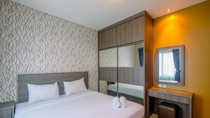 A neatly made bed with white linens and two rolled towels, a wooden headboard, a mirror above the bed, and a small wooden bench with a mirror.