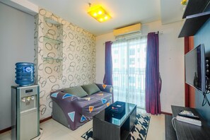 A living room with a sofa, a water dispenser, a flat-screen TV, and a window with curtains.