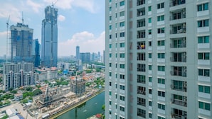 A high-rise building with multiple floors and balconies, surrounded by other buildings and a river.
