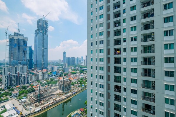 A high-rise building with multiple floors and balconies, surrounded by other buildings and a river.