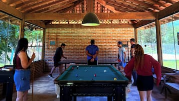 Mesa de bilhar em área coberta, com paredes de tijolo e vigas de madeira.