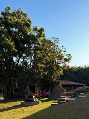 A grassy area with a hammock, a wooden structure, and a building with a tiled roof. - Hotel Campestre Atibaia (Atibaia)