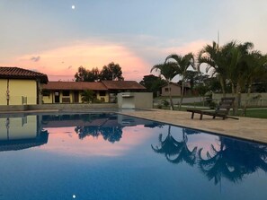 A swimming pool with clear water reflecting palm trees and a sunset sky. - Hotel Campestre Atibaia (Atibaia)