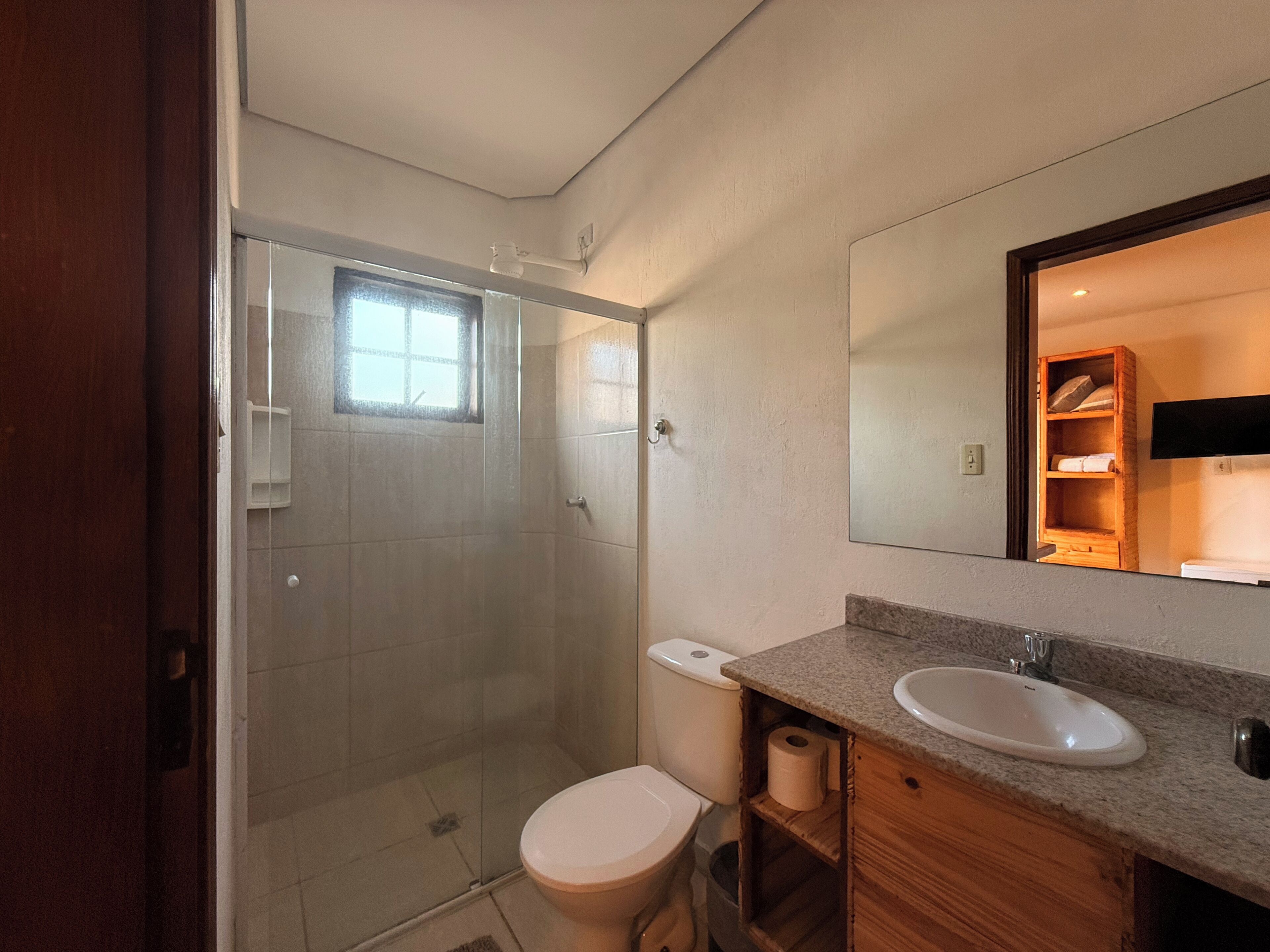 A bathroom with a shower, toilet, sink, and a wooden cabinet.