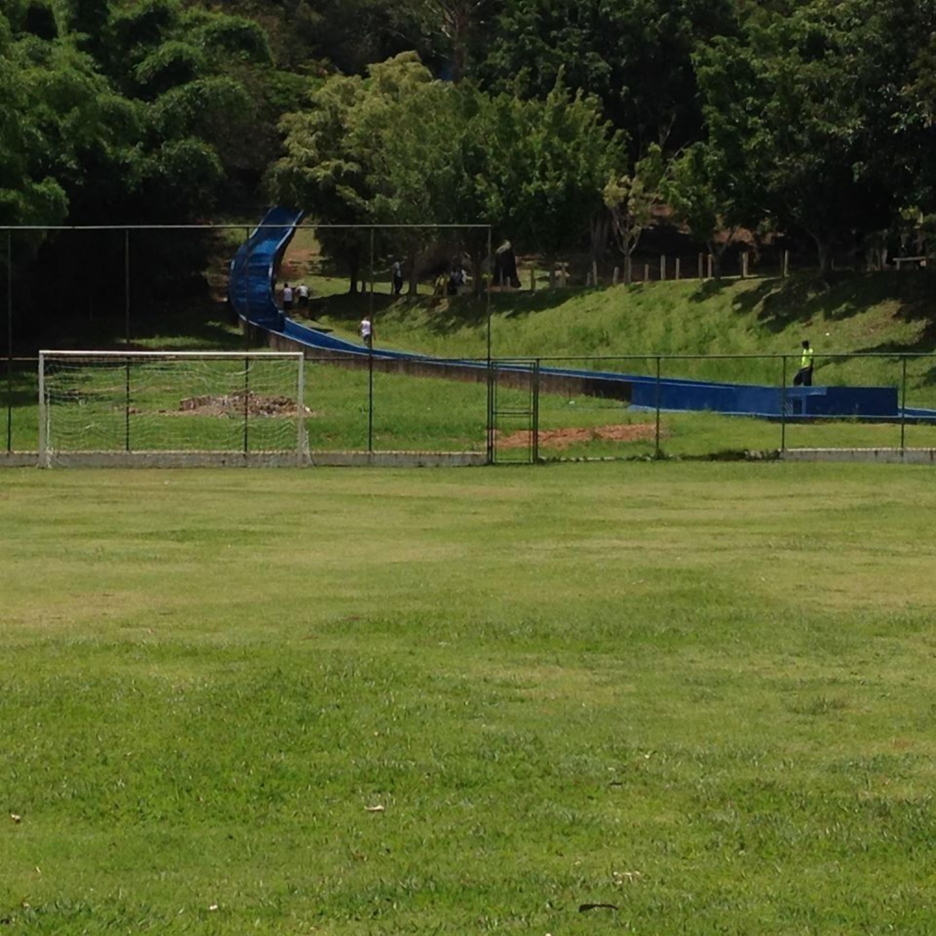 Uma longa trilha azul e sinuosa em um campo gramado, com um gol de futebol e árvores ao fundo.