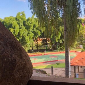 A view of a sports court with a basketball hoop, surrounded by trees and a building with a red roof. - Hotel Campestre Atibaia (Atibaia)