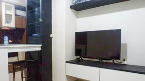 A modern kitchen with a black countertop, a TV mounted on the wall, and a bar stool. - Exquisite 1BR at Praxis Apartment (Surabaya)