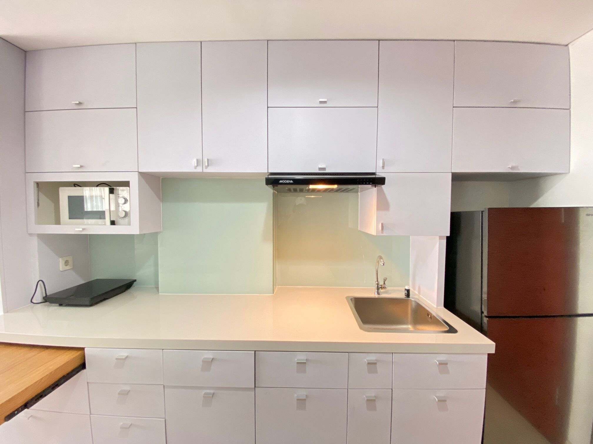 A modern kitchen with white cabinets, a stainless steel sink, a microwave, and a refrigerator.