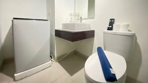 Un baño pequeño y limpio con inodoro, lavamanos y refrigerador blancos.