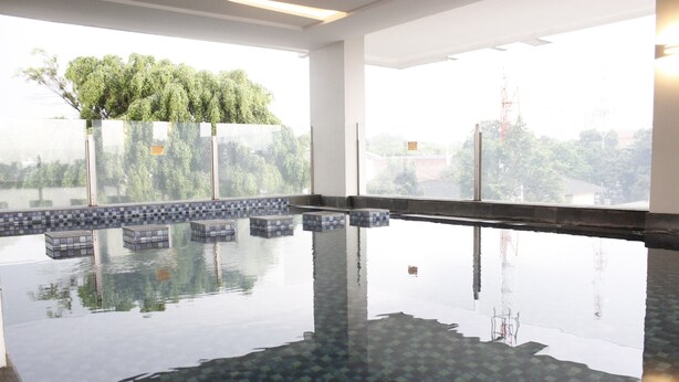 Una piscina interior con paredes de vidrio transparente, suelo de baldosas y vistas a árboles y edificios al exterior.