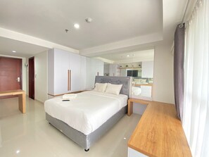 A modern bedroom with a large bed, a wooden nightstand, a wardrobe, and a mirror. - Modern & Comfy Studio Apartment at Tamansari Tera Residence (Bandung)