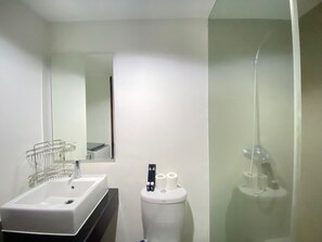 A modern bathroom with a white sink, a toilet, and a glass shower enclosure. - Modern & Comfy Studio Apartment at Tamansari Tera Residence (Bandung)