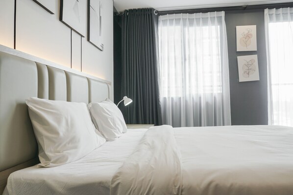 A neatly made bed with white linens, a headboard with a light finish, and two framed artworks on the wall. - Comfort Studio at Daan Mogot City Apartment (Jakarta)