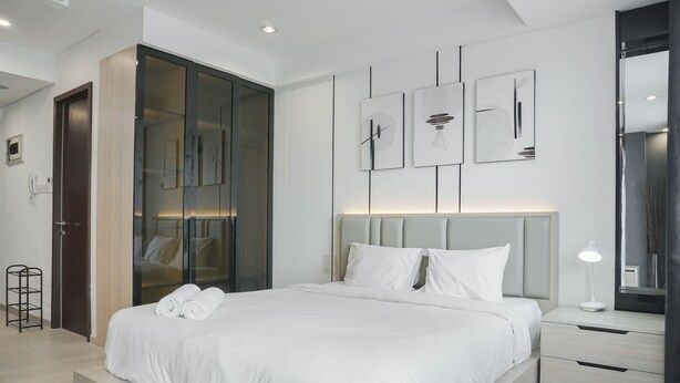 A modern bedroom with a large bed, a walk-in closet, and a bedside table with a lamp.