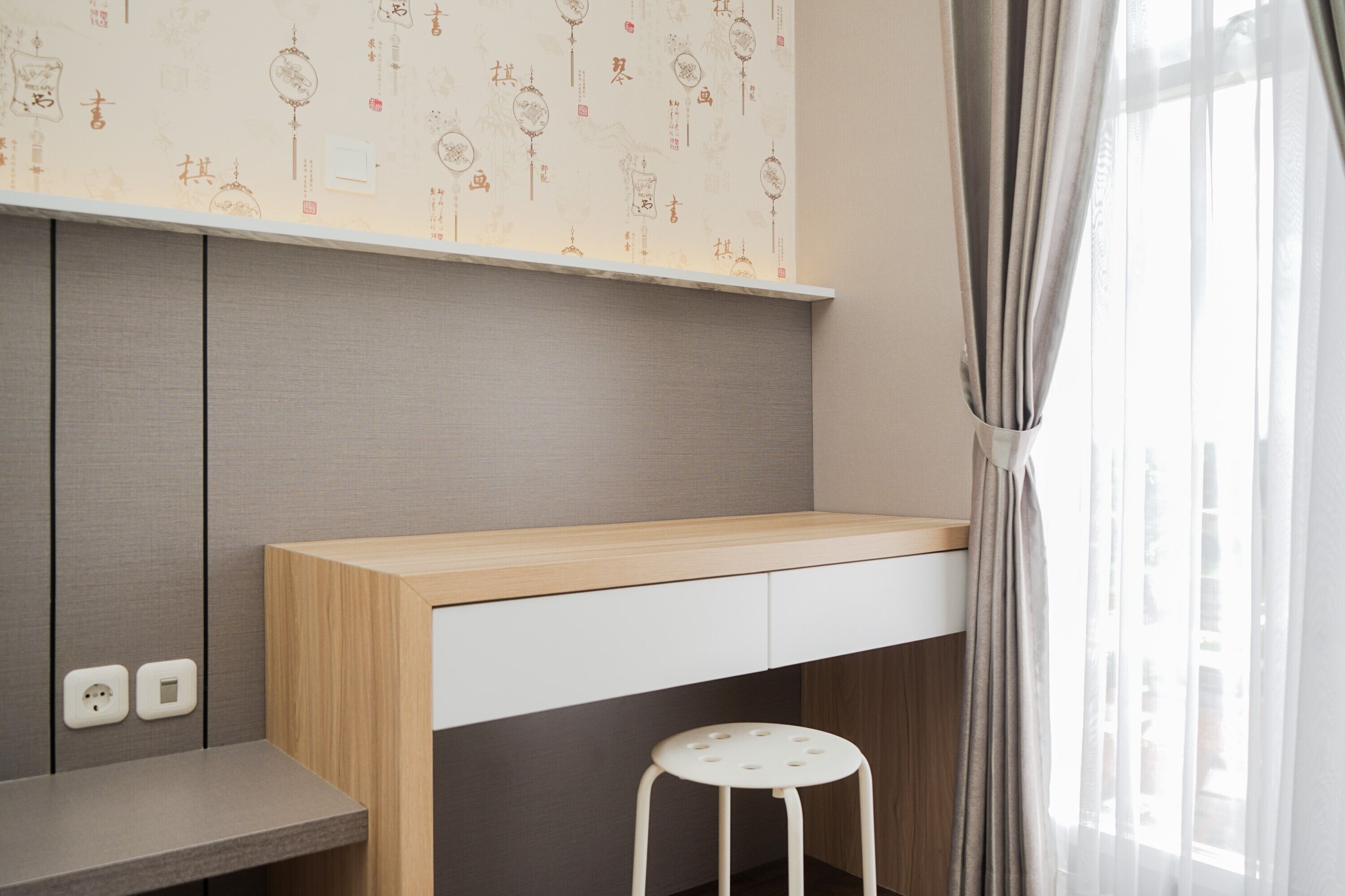 Una habitación moderna con un escritorio de madera, un taburete blanco y una pared con diseños decorativos.