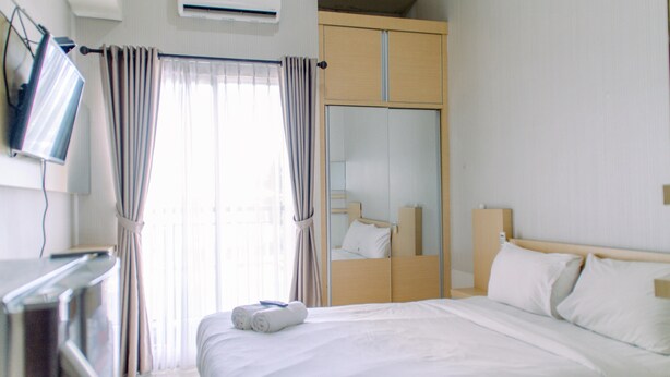 A hotel room with a bed, a TV, a wardrobe, and a window with curtains. - Nice and Comfy Studio Room at Serpong Greenview Apartment (South Tangerang)