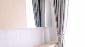 A minimalist room with a wooden shelf and a mirror reflecting curtains. - Nice and Comfy Studio Room at Serpong Greenview Apartment (South Tangerang)