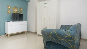 A room with a white wardrobe, a blue sofa with yellow lines, and a white cabinet with a TV.