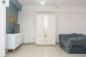 A room with a white wardrobe, a blue sofa, and a TV on a white cabinet. - Best and Strategic Studio at Bassura Apartment (Jakarta)