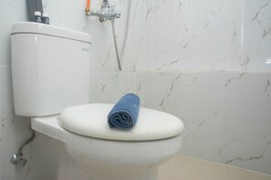 A toilet with a blue towel on the seat, a showerhead, and a toilet paper holder. - Best and Strategic Studio at Bassura Apartment (Jakarta)