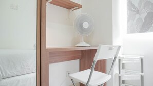 A room with a bed, a desk with a white fan, a white chair, and a white shelving unit. - Restful and Tidy 2BR at Green Pramuka City Apartment (Jakarta)