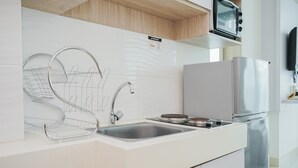 A modern kitchen with a stainless steel sink, a dish drying rack, a microwave, and a refrigerator. - Comfy and Nice 1BR at Tree Park City BSD Apartment (South Tangerang)