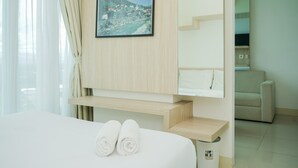 A hotel room with a bed, a framed picture of a coastal town, and a neatly made bed with rolled towels. - Comfy and Nice 1BR at Tree Park City BSD Apartment (South Tangerang)