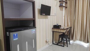 A compact room with a refrigerator, a television mounted on the wall, a small table with a chair, and a window with curtains. - Comfort Studio at Vida View Makasar Apartment (Makassar)