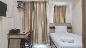 A hotel room with a bed, a desk with a chair, a television mounted on the wall, and curtains. - Comfort Studio at Vida View Makasar Apartment (Makassar)