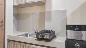 A compact kitchen with a gas stove, a sink, and a stainless steel refrigerator. - Comfort Studio at Vida View Makasar Apartment (Makassar)