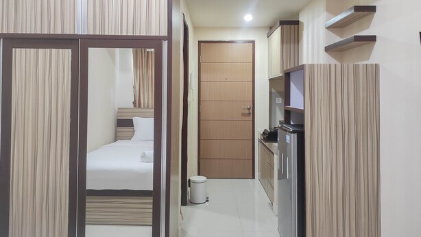 A narrow hallway with a bed, a door, and a trash bin. - Comfort Studio at Vida View Makasar Apartment (Makassar)
