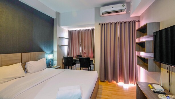 A hotel room with a bed, desk, chairs, TV, and an air conditioning unit. - Cozy Living and Homey Studio Apartment at Margonda Residence 5 (Depok)