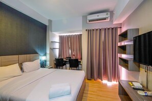A hotel room with a bed, desk, chairs, TV, and an air conditioning unit. - Cozy Living and Homey Studio Apartment at Margonda Residence 5 (Depok)