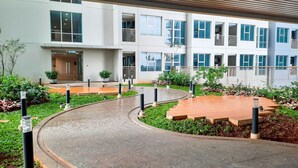 Un edificio moderno con un camino curvo, plantas en macetas y una zona con terraza de madera.