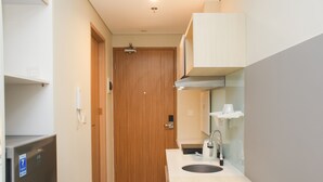 Un pasillo estrecho que conduce a una puerta de madera, una kitchenette con fregadero y estufa, y un refrigerador a la izquierda.