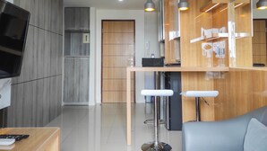A modern kitchen with wooden cabinets, a built-in oven, and a bar area with stools. - Spacious 2BR at Vida View Makassar Apartment (Makassar)