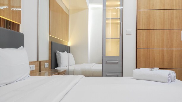 A modern hotel room with a large bed, a bedside table, a nightstand, a wardrobe, and a mirror. - Spacious 2BR at Vida View Makassar Apartment (Makassar)
