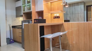 A modern kitchen with wooden cabinets, a built-in oven, and a bar area with stools. - Spacious 2BR at Vida View Makassar Apartment (Makassar)
