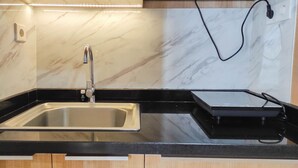 A kitchen with a stainless steel sink, black countertop, and marble backsplash. - Spacious 2BR at Vida View Makassar Apartment (Makassar)