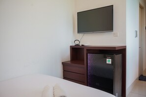 A hotel room with a bed, a TV mounted on the wall, a small refrigerator, and a wooden cabinet.