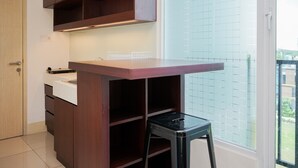 A compact kitchen with wooden cabinets, a countertop, and a stool. - Comfy and Nice Studio at Tree Park City BSD Apartment (South Tangerang)