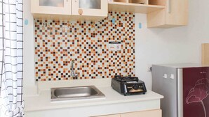A kitchen with a tiled backsplash, a sink, a stove, and wooden cabinets. - Simple and Cozy Living Studio Room at Bassura City Apartment (Jakarta)