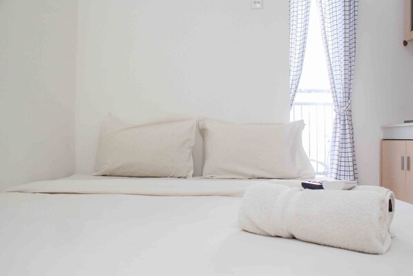 A neatly made bed with a white duvet, pillows, and a rolled white towel.