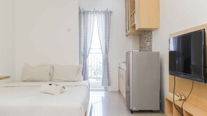 A small, clean room with a bed, a refrigerator, a TV, and a window with curtains. - Simple and Cozy Living Studio Room at Bassura City Apartment (Jakarta)