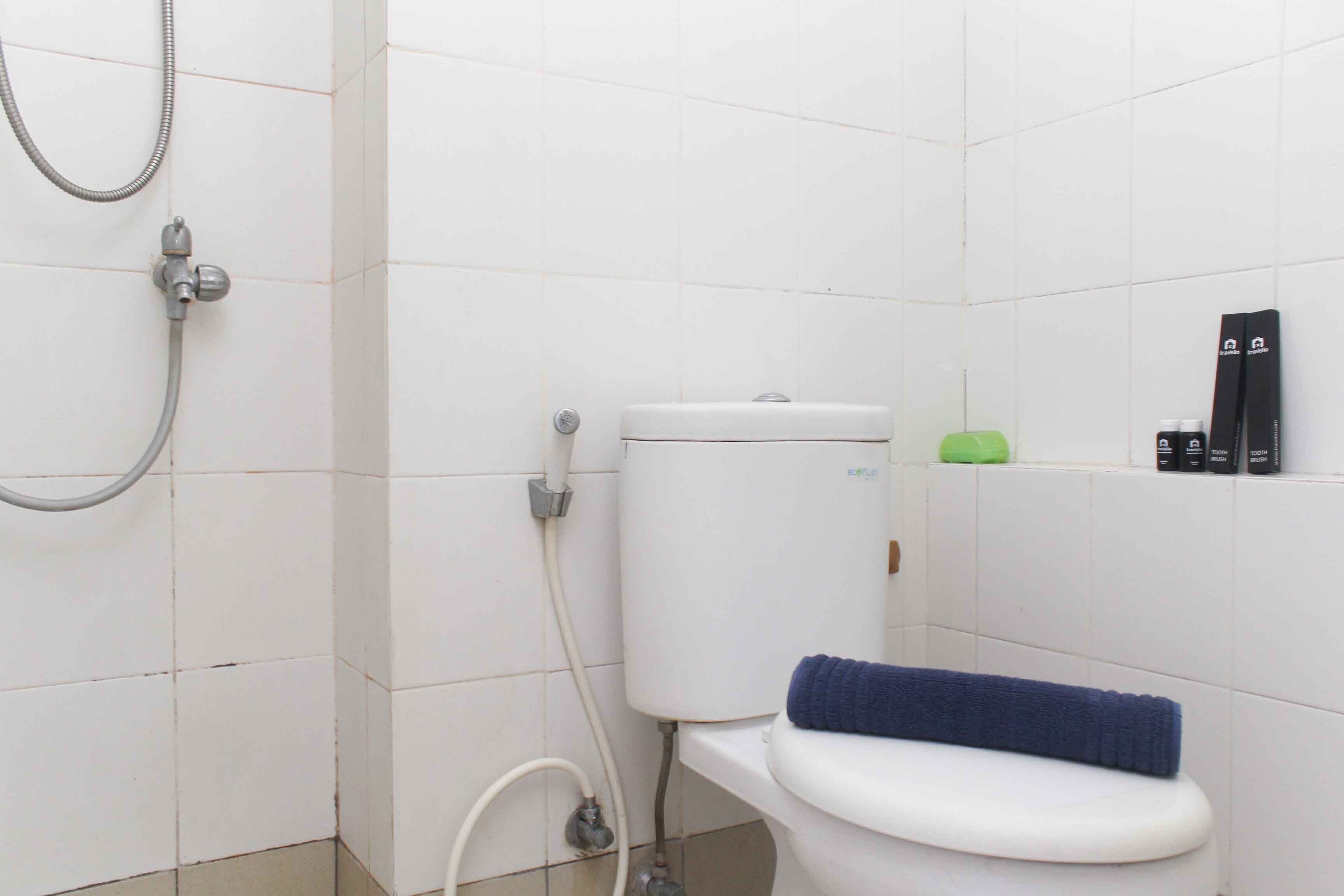 A small bathroom with a white toilet, a shower head, and a green bottle on the wall.