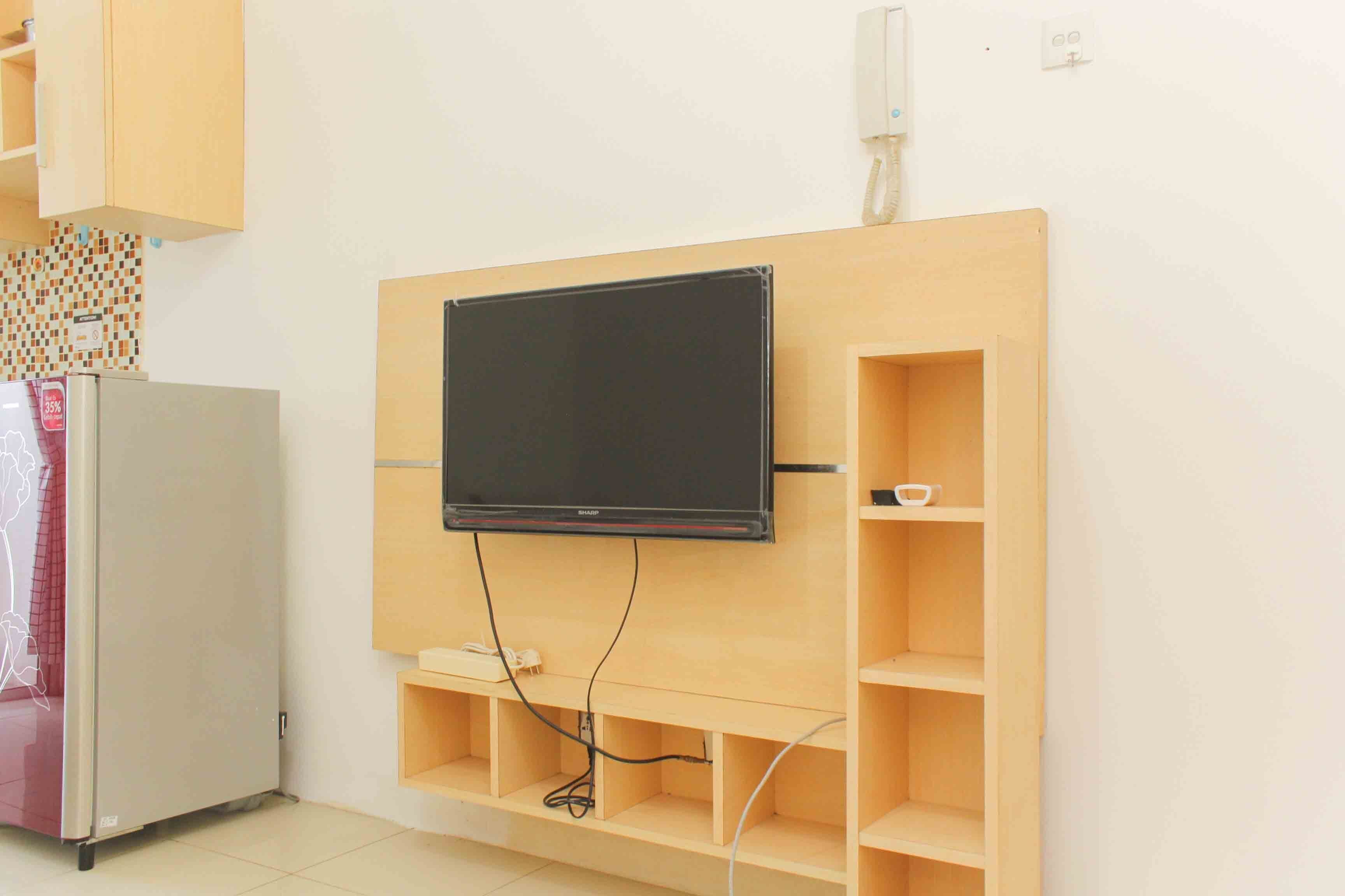 Une pièce avec un téléviseur fixé au mur, un mur en bois, un réfrigérateur blanc et un pare-feu en carreaux.