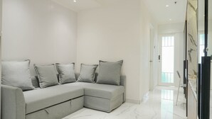 A modern living room with a grey sectional sofa, a glass cabinet, and a marble floor. - Comfortable and Simply 1BR at The Boulevard Apartment (Jakarta)