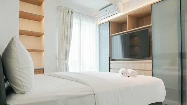 A modern hotel room with a large bed, a flat-screen TV, and a sliding glass door leading to a balcony. - Comfortable and Simply 1BR at The Boulevard Apartment (Jakarta)