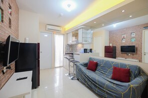 A modern living room with a sofa, a TV, a kitchen area, and a brick wall.